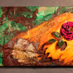 a moldy, partially flattened, decaying jack-o-lantern laying in a bed of bright green foliage; one eye of the jack-o-lantern has a high-relief pink rose with leaves protruding outward