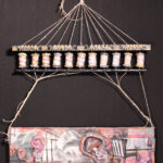 a wooden panel with three prominent ear sculptures, and linear black and white magazine images of a window and living room furniture are collaged onto a narrow horizontal wood panel with orange, magenta, violet and light blue-tinted encaustic medium found quotes are embeded along the edge and one saying "talent has hunger" is printed on a thin piece of paper like a fortune cookie; the wooden panel is suspended from spiderweb-like twine configure above into a carousel-like prayer wheel formation above made of found objects