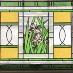 finished Iris Window with detailed organic center showing two white Irises, one taller than the other surrounded densely by light and dark green leaves; the colors from the Iris panel are repeated in the stripes above and below and in the rectangular panels at either side; beveled squares and rectangles border the Iris panel and decorate the left and right edges of the window