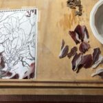 cut pieces of glass freshly cleaned of their template paper are being arranged over top of their respective portions of the sketch