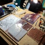 sheets of glass with pieces of the brown template paper cut and glued onto them in preparation for cutting and grinding