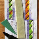 sketches of long vertical closet door glass with stacked triangular motifs, one sketch capturing the color of the glass lit from the front and the other capturing the drastically different colors that show when backlit; samples of the glass to be used in the project are laid on top