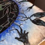 a collection of different sized, hands all in different positions with tree-bark like coloring and texturing are in a silhouetted grassy brambly field wiht sunset colors behind in the sky; the hands are protruding inward from a square substrate and encircling a stained glass circular image of the sky with the Aurora Borealis and moon at the center; the fingertips of the hands turn into tree branches that have lines of poetry resting on them; where the branches reach the glass sky, they become the poetry coated in colorful ice as though a tree after an ice storm, being lit by the Northern Lights