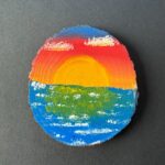 Rustic round live-edge coaster with a sunset over rippled water painted on the surface