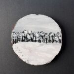 Rustic round live-edge coaster with a monochromatic snowy, densely tree-lined field that has a subtle path of footprints headed into the woods painted on the surface