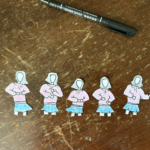 Five drawing cutouts of the same character with shoulder-length hair, no face, a pink sweatshirt and a blue skirt; each drawing has her body in a slightly different position to make it look as though she is dancing