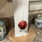 Ladybug sculpted with plaster gauze and decorated with acrylic paint and curly wire antennas that is suspended from a string to be a paper towel weight