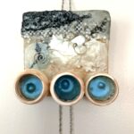 a square relief mixed media painting with a black and white mass of woven jewelry at the top appearing to deteriorate, with beads scattered downward into a smoother, cream beige and white central section with black decorative hands of a clock and a spiral whirling around it; at the bottom are mounted in a row three bisqueware vessels each painted inside with bright metallic blue and each with a bubble-like bulge resting in the center