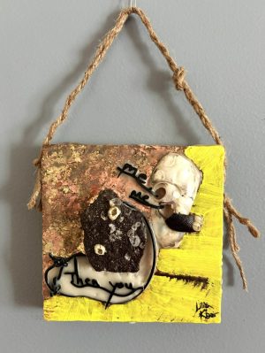 a square low-relief mixed media painting divided in half by a collection of found beach objects each with a notable pair of holes, as well as black leather cord and black text reading "me," "me," "Then you"; the background of the top left is gold and copper leaf and of the bottom right is bright yellow