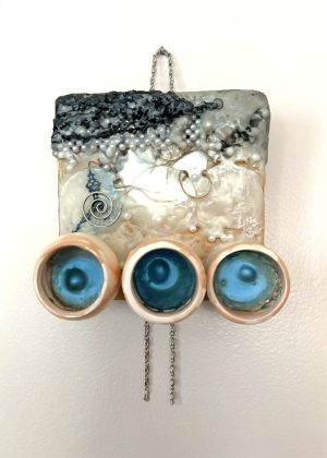 a square relief mixed media painting with a black and white mass of woven jewelry at the top appearing to deteriorate, with beads scattered downward into a smoother, cream beige and white central section with black decorative hands of a clock and a spiral whirling around it; at the bottom are mounted in a row three bisqueware vessels each painted inside with bright metallic blue and each with a bubble-like bulge resting in the center