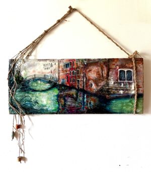 a Venetian canal with a woman face lying on the surface of the olive green and teal water facing upward toward the left and the image of a man's face overlaid on the burgundy, gray, cranberry, and orange-colored buildings facing downward and toward the right